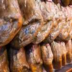 lines of shiny cured iberico ham hanging legs. spain