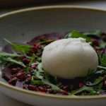 Fresh burrata cheese on beet salad with arugula and pomegranate seeds.