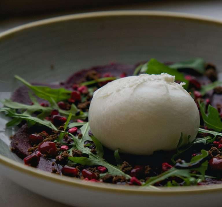 Fresh burrata cheese on beet salad with arugula and pomegranate seeds.