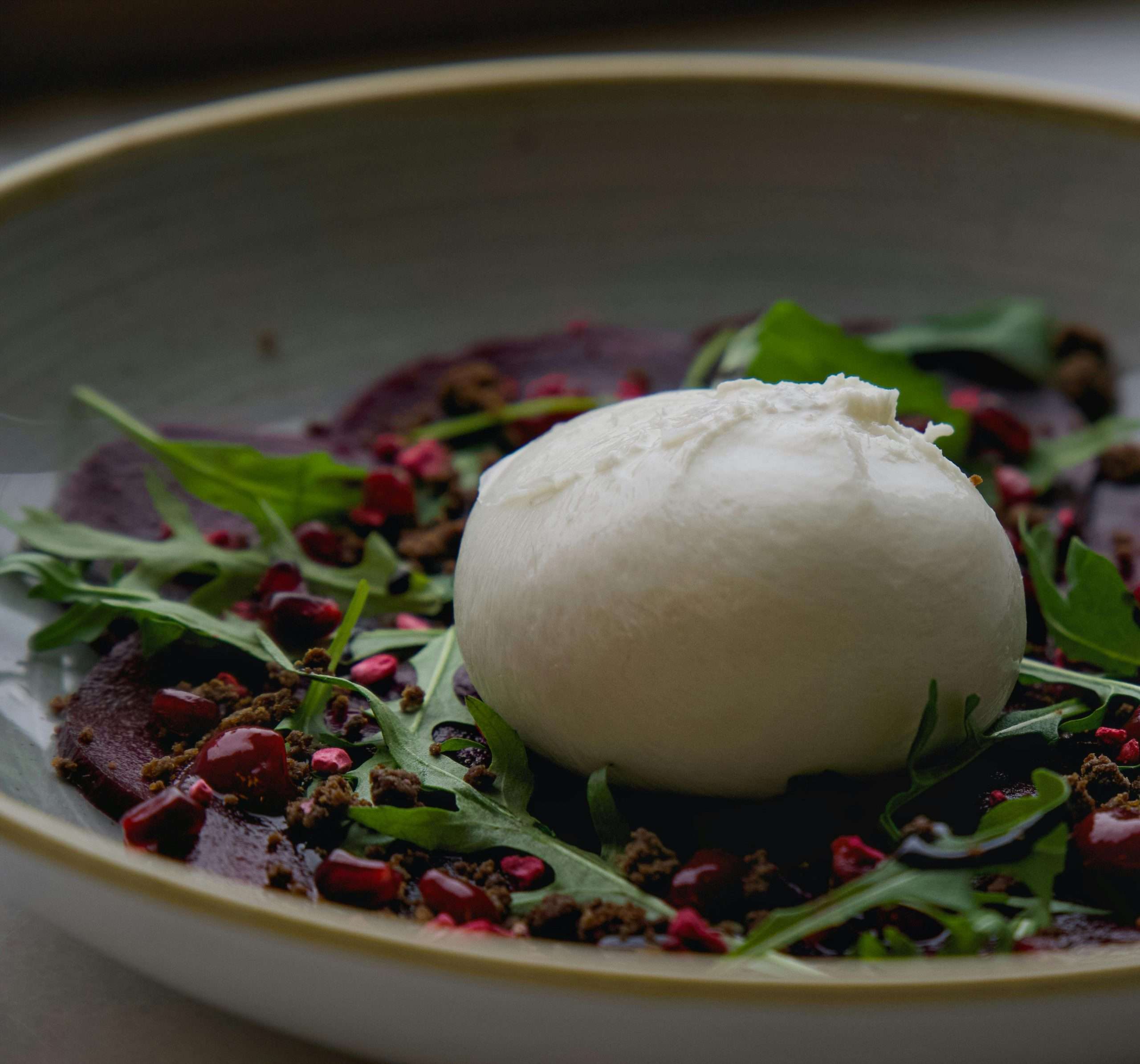 Fresh burrata cheese on beet salad with arugula and pomegranate seeds.