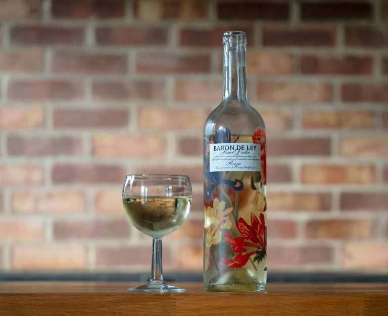 A Baron de Ley wine bottle and glass on a wooden table with a brick wall background.